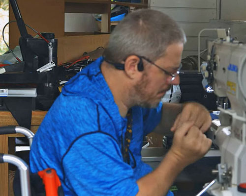 Picture shows Dave Shraga using a sewing machine to make gloves for wheelchair users.